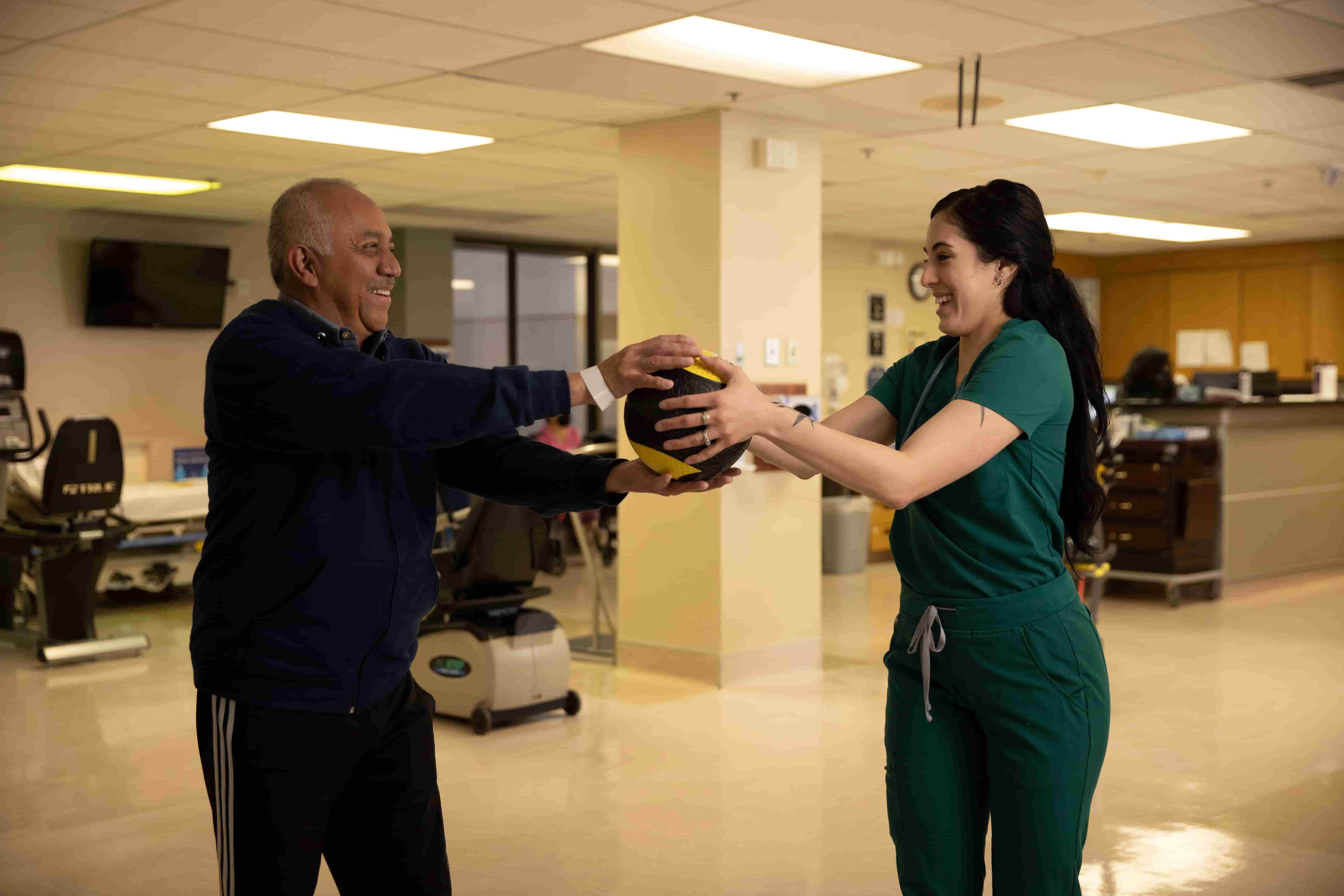 Rehabilitation therapist assisting an older patient with an exercise.